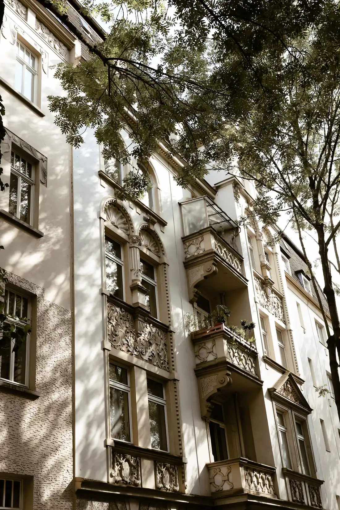 Verzierte Altbaufassade mit Balkonen, teilweise von Baumzweigen verdeckt